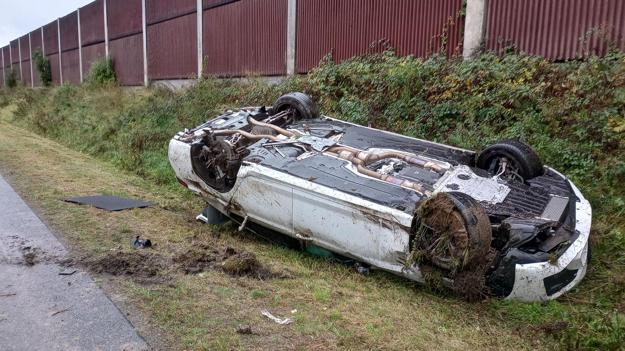 Ein umgestürztes Auto liegt auf dem Rücken einer Grünfläche bei einer Autobahn.