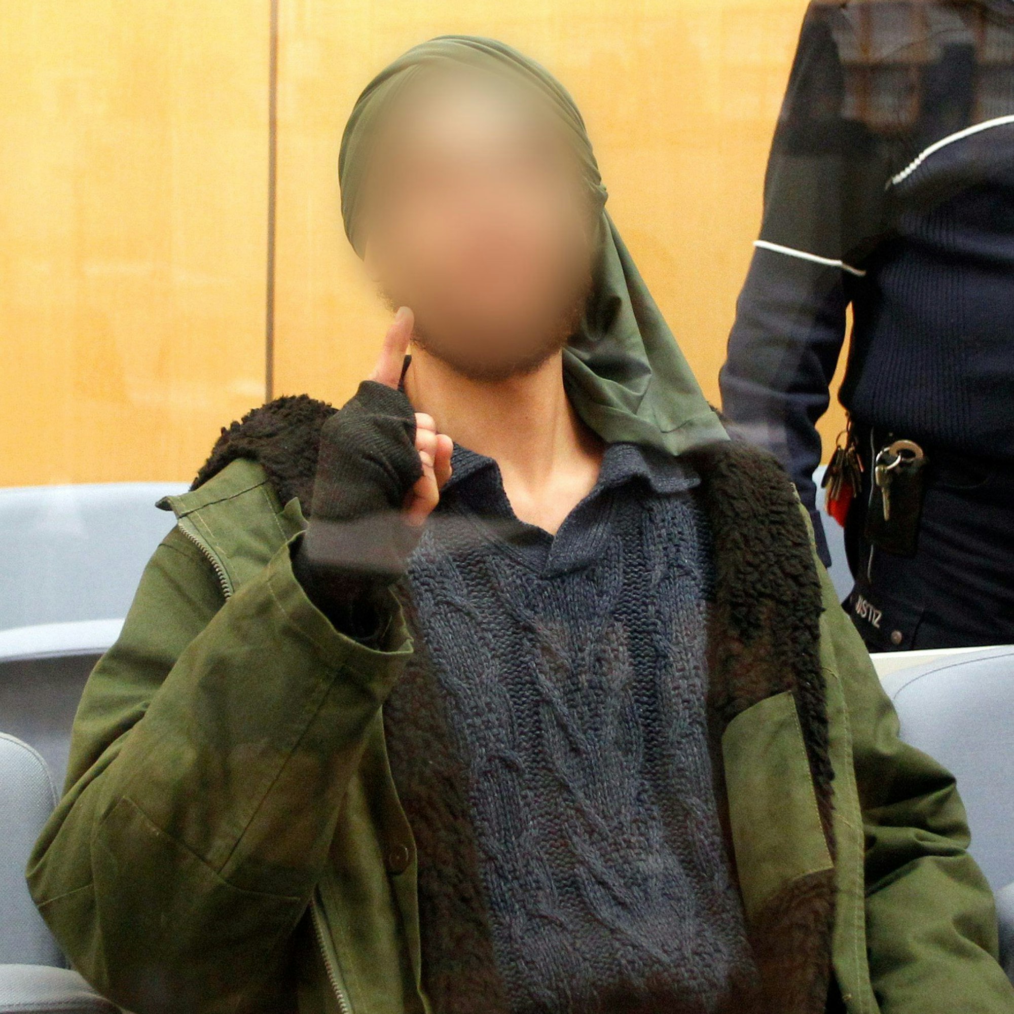 ARCHIV - 22.12.2016, Nordrhein-Westfalen, Düsseldorf: Der Angeklagte wartet hinter einer Sicherheitsscheibe vor dem Oberlandesgericht auf den Prozessbeginn. Er wurde am 6. April 2017 als IS-Terrorist vom Düsseldorfer Oberlandesgericht zu fünf Jahren Jugendhaft verurteilt. Gegen den am 24.10. in Duisburg festgenommenen vorbestraften Islamisten ist Haftbefehl erlassen worden, teilte die Generalstaatsanwaltschaft Düsseldorf am Mittwoch mit. Der 29-Jährige soll sich gegenüber einem Chatpartner in Syrien zur Begehung eines islamistisch motivierten Anschlags auf eine pro-israelische Demonstration bereiterklärt haben. Foto: picture alliance / Roland Weihrauch/dpa - ACHTUNG: Das Gesicht des Angeklagten wurde auf Verfügung des Gerichts gepixelt. +++ dpa-Bildfunk +++