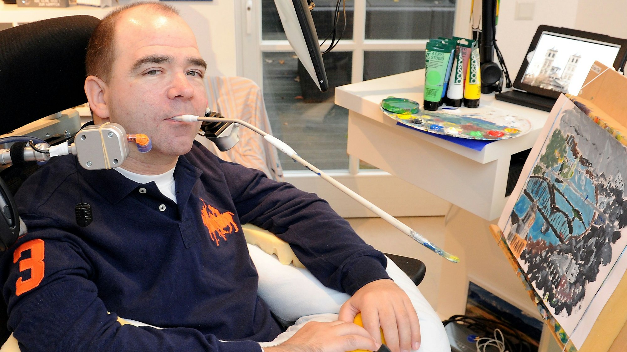 Zu sehen ist Rainer Broicher, der ein mundgemaltes Bild vor sich hat.