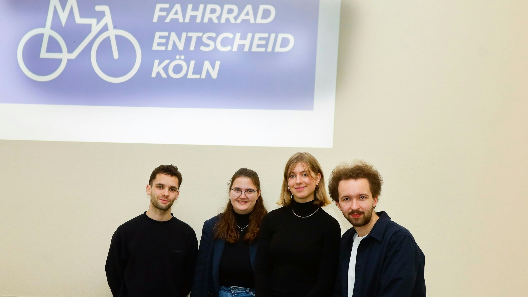 Zwei junge Männer und zwei Junge Frauen vor einem Plakat mit der Aufschrift „Fahrrad-Entscheid-Köln“.