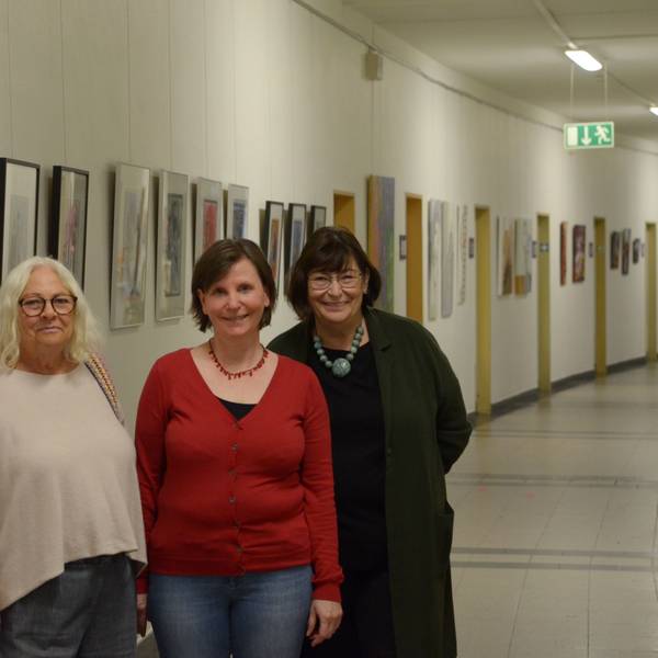Die Künstlerinnen Donata Reinhard (v.l.), Petra Hansen und Beate Krupp stehen in einem der Flure des Euskirchener Rathauses, in denen sie ihre Werke ausstellen. Im Hintergrund hängen zahlreiche Bilder.