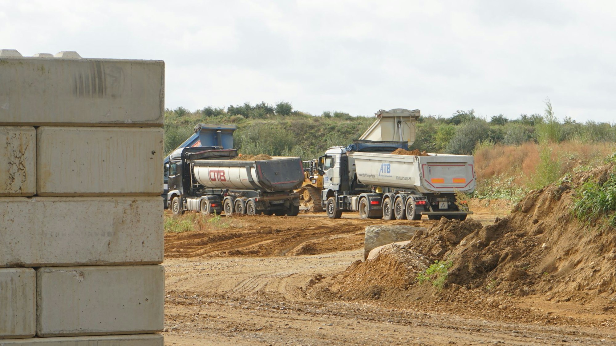 Vier Lastwagen kippen Kies in eine Grube.
