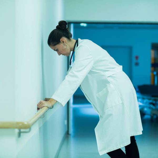 Eine gestresste Ärztin stützt sich im Krankenhausflur an einem Handlauf ab.