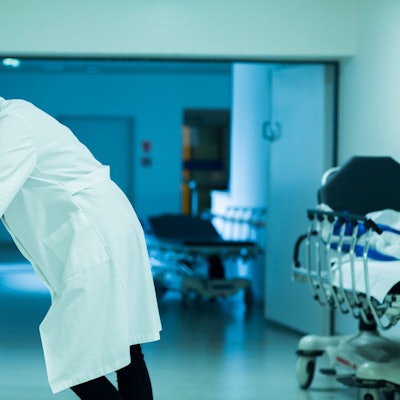 Eine gestresste Ärztin stützt sich im Krankenhausflur an einem Handlauf ab.