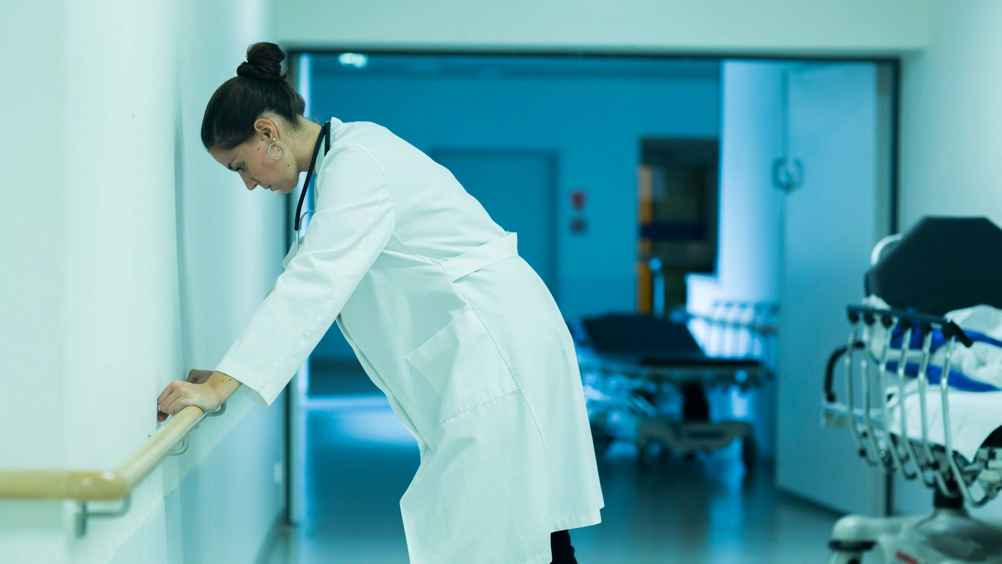 Eine gestresste Ärztin stützt sich im Krankenhausflur an einem Handlauf ab.