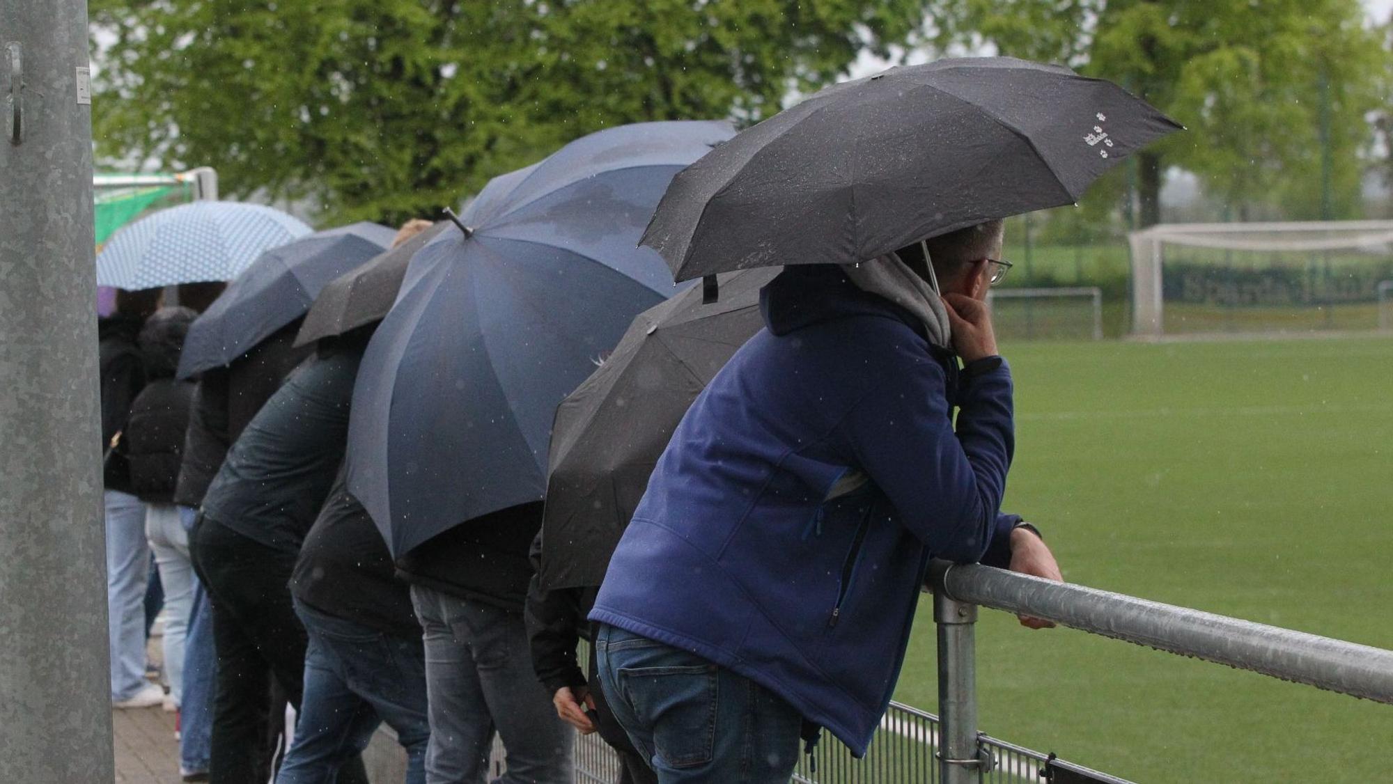 Zuschauer betrachten unter Regenschirmen ein Fußballspiel