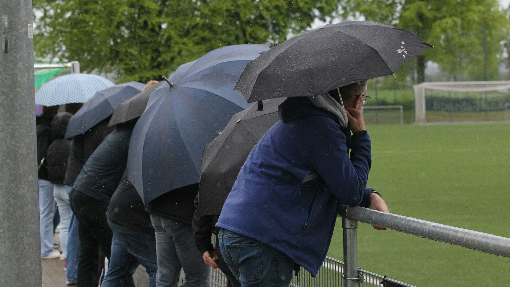 Zuschauer betrachten unter Regenschirmen ein Fußballspiel