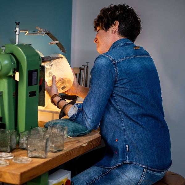 Kerstin Wexel nutzt eine Maschine, um Glas zu gestalten. Sie schaut dabei auf das Stück in Bearbeitung.
