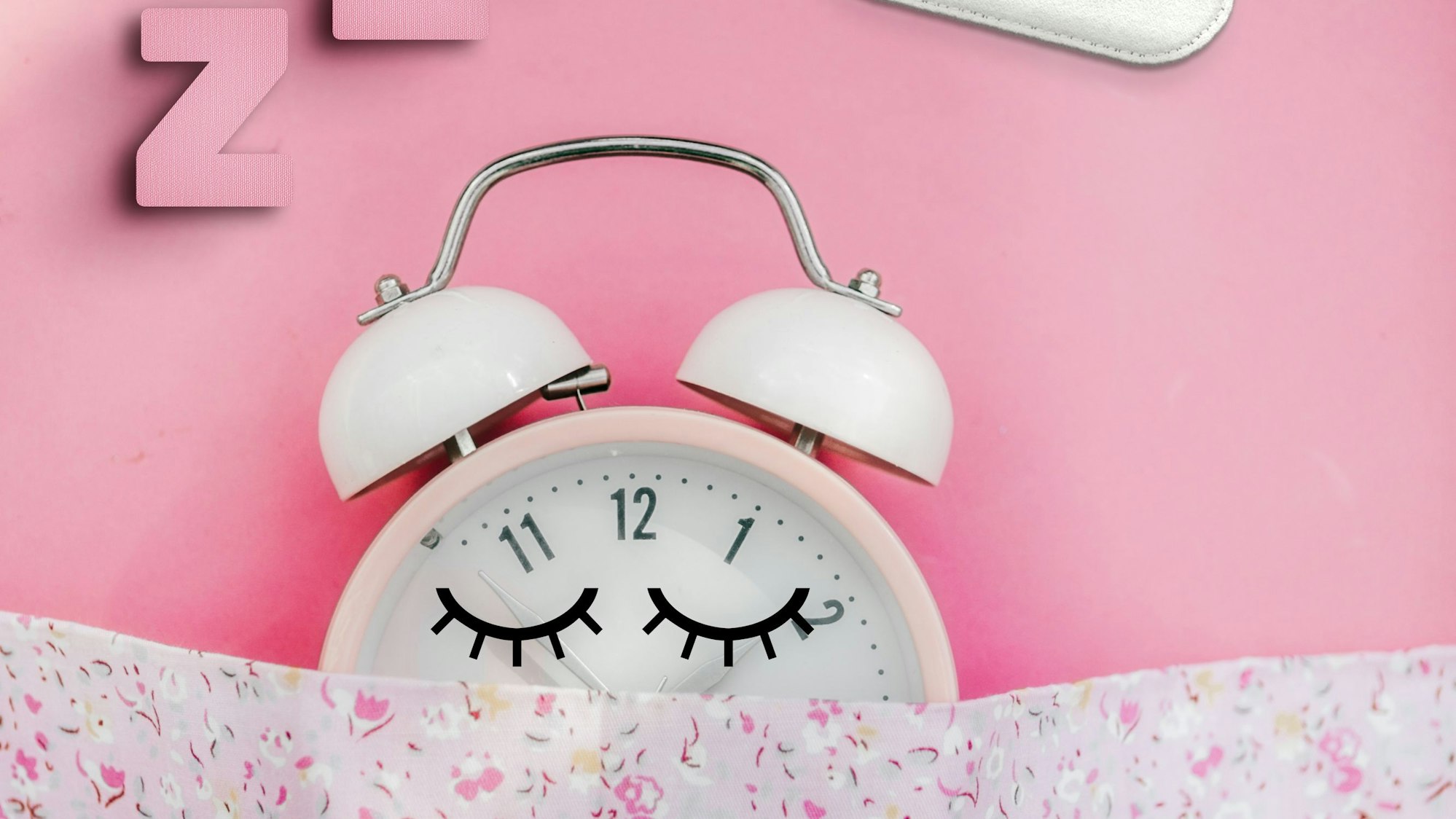 Ein Wecker liegt unter einer Decke und schläft