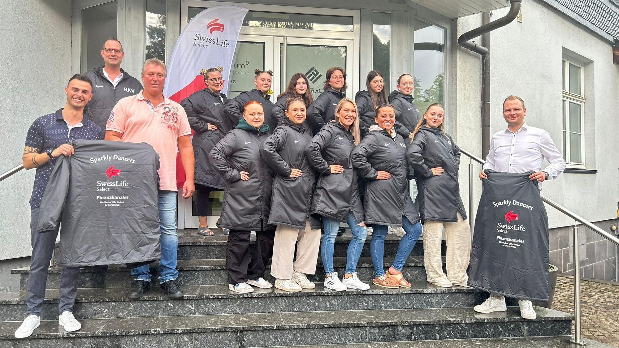 Eine Tanzgruppe steht für ein Gruppenbild gemeinsam auf Treppenstufen beisammen und präsentiert die neue gesponsorte Kleidung.