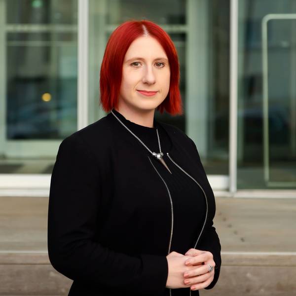 Lydia Benecke trägt ein schwarzes Kleid und eine schwarze Jacke und blickt in die Kamera