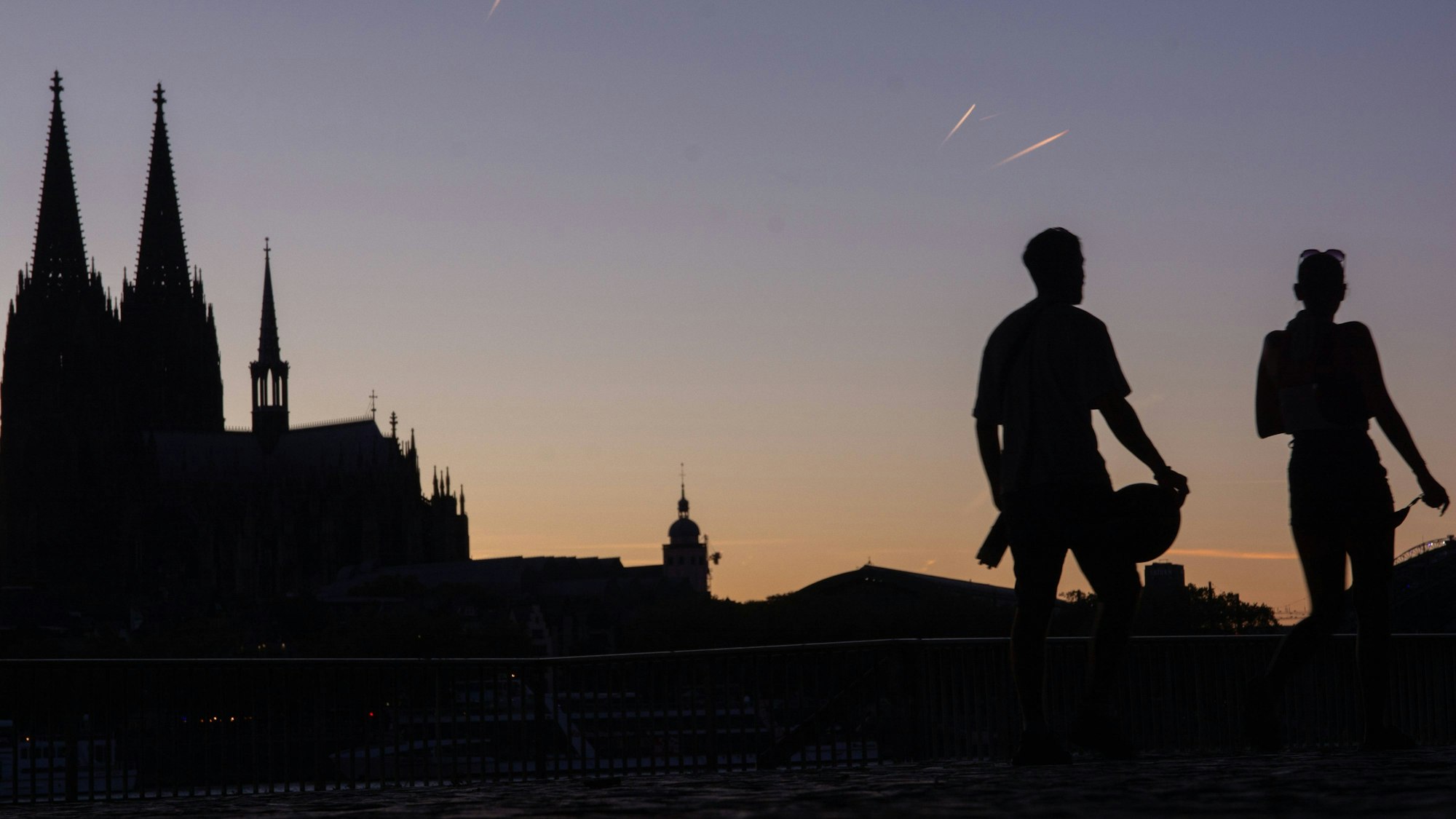 Sonnenuntergang in Köln, zwei Menschen spazieren am Kölner Dom vorbei.