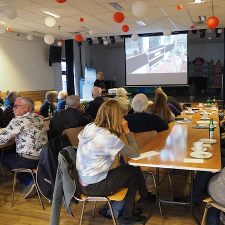 Ein Mann hält einen Vortrag, die Zuhörer schauen auf eine Leinwand.