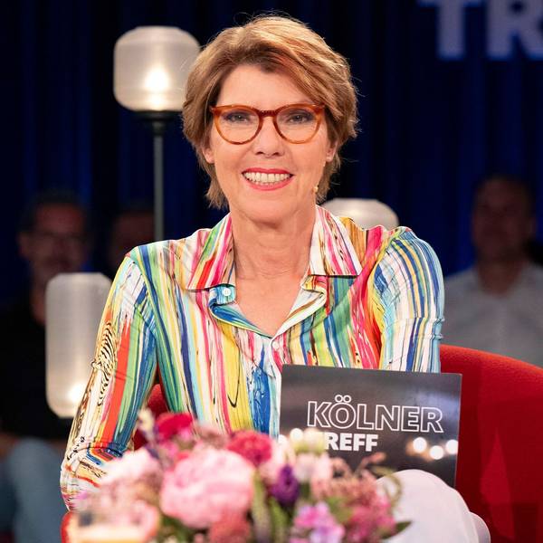 Moderatorin Bettina Böttinger sitzt im Studio des „Kölner Treff“. Sie trägt eine bunt gemusterte Bluse und blickt lächelnd in die Kamera.
