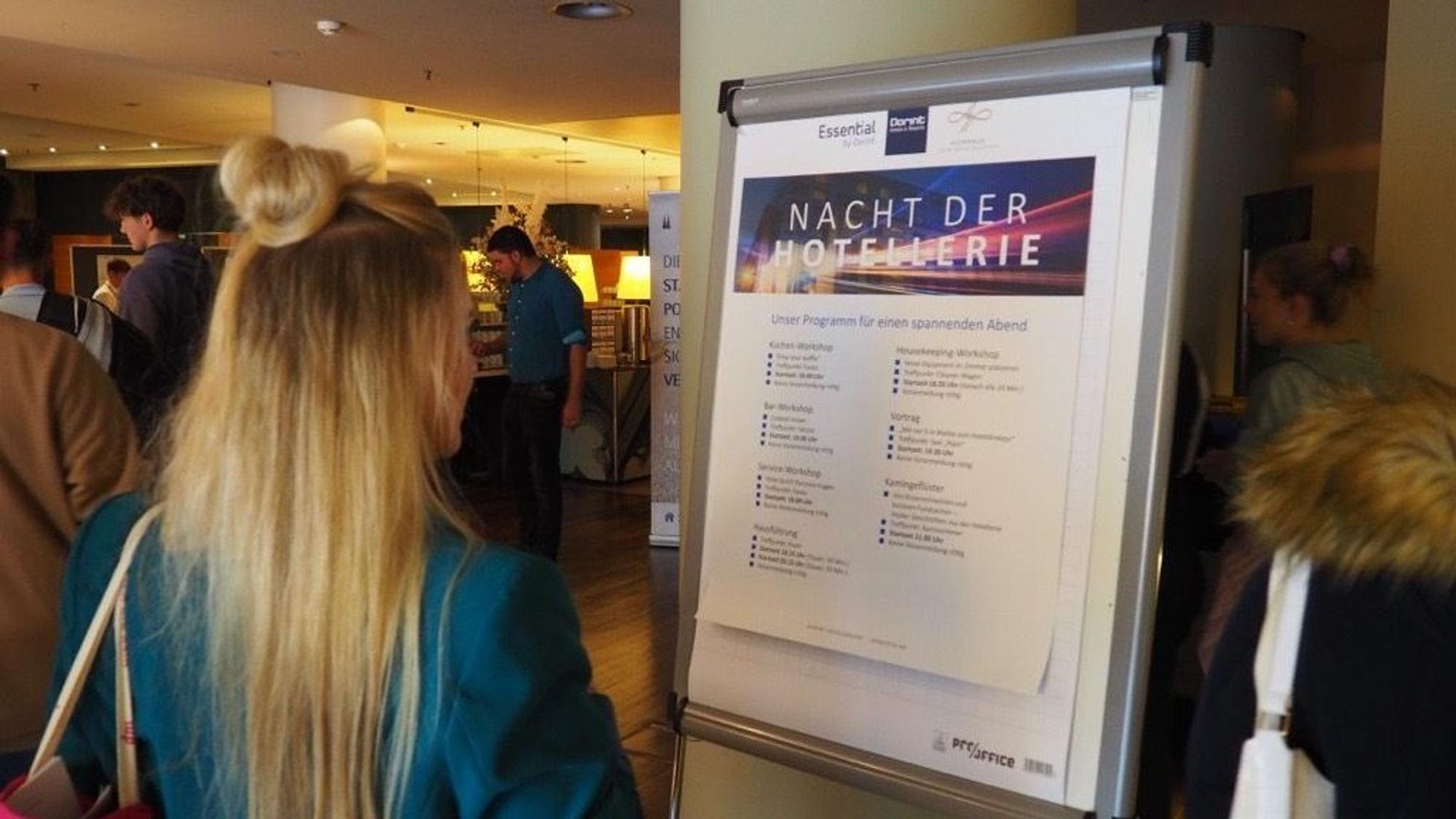 Zu sehen ist eine Frau die auf den Austeller mit den verschiedenen Erlebnisworkshops schaut