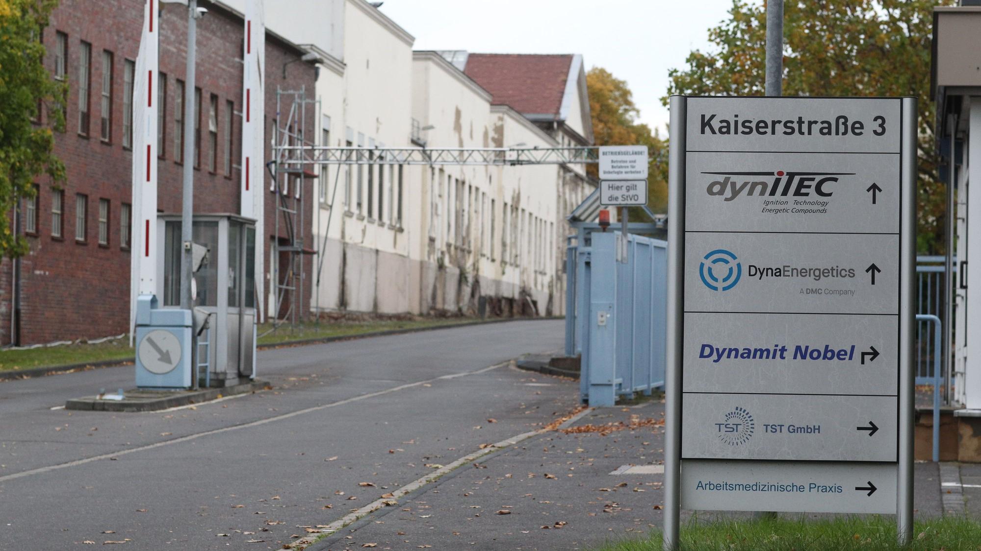 Die Zufahrt zu einem Industriegelände. Links stehen Fabrikgebäude, rechts eine Informationssäule mit den Namen ansässiger Firmen.