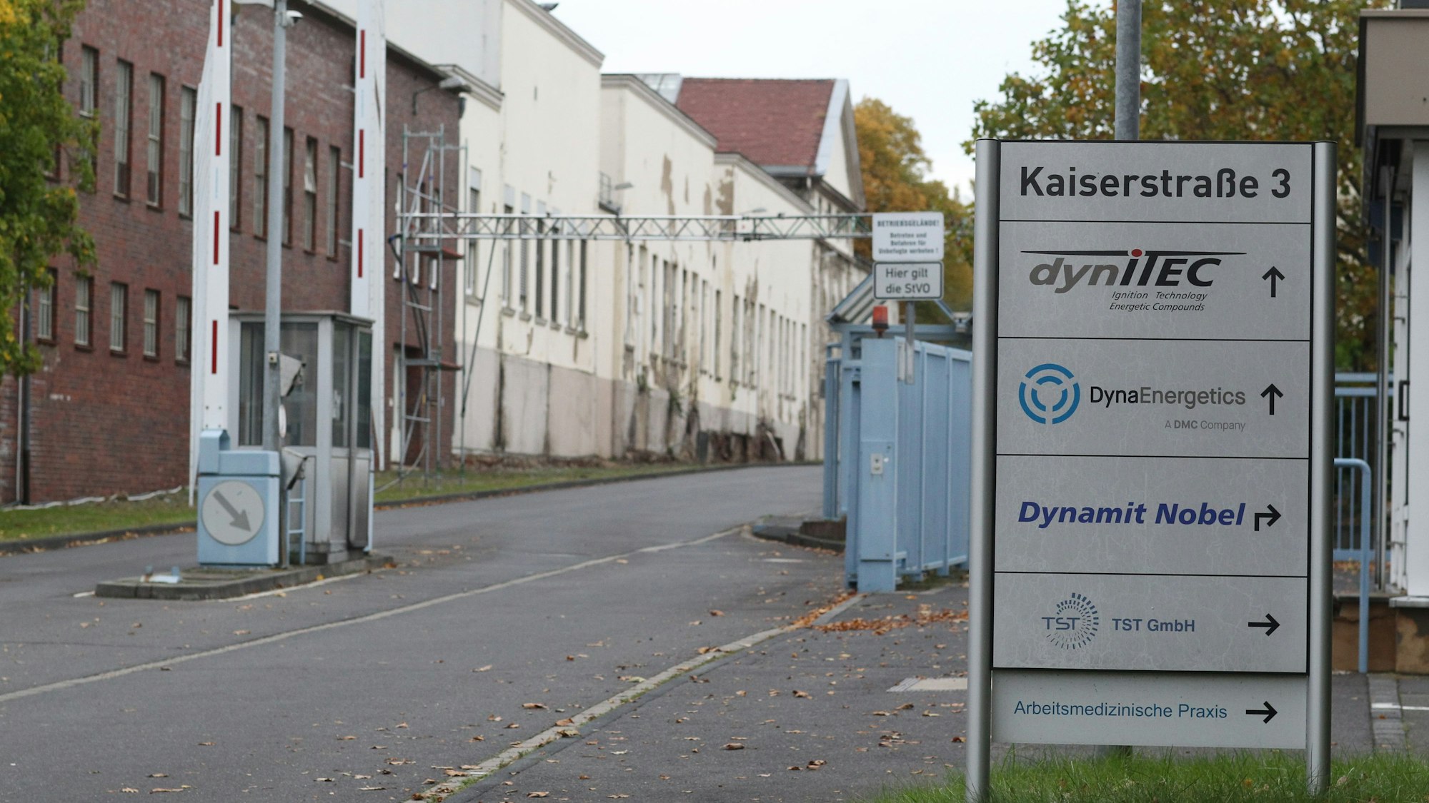 Die Zufahrt zu einem Industriegelände. Links stehen Fabrikgebäude, rechts eine Informationssäule mit den Namen ansässiger Firmen.