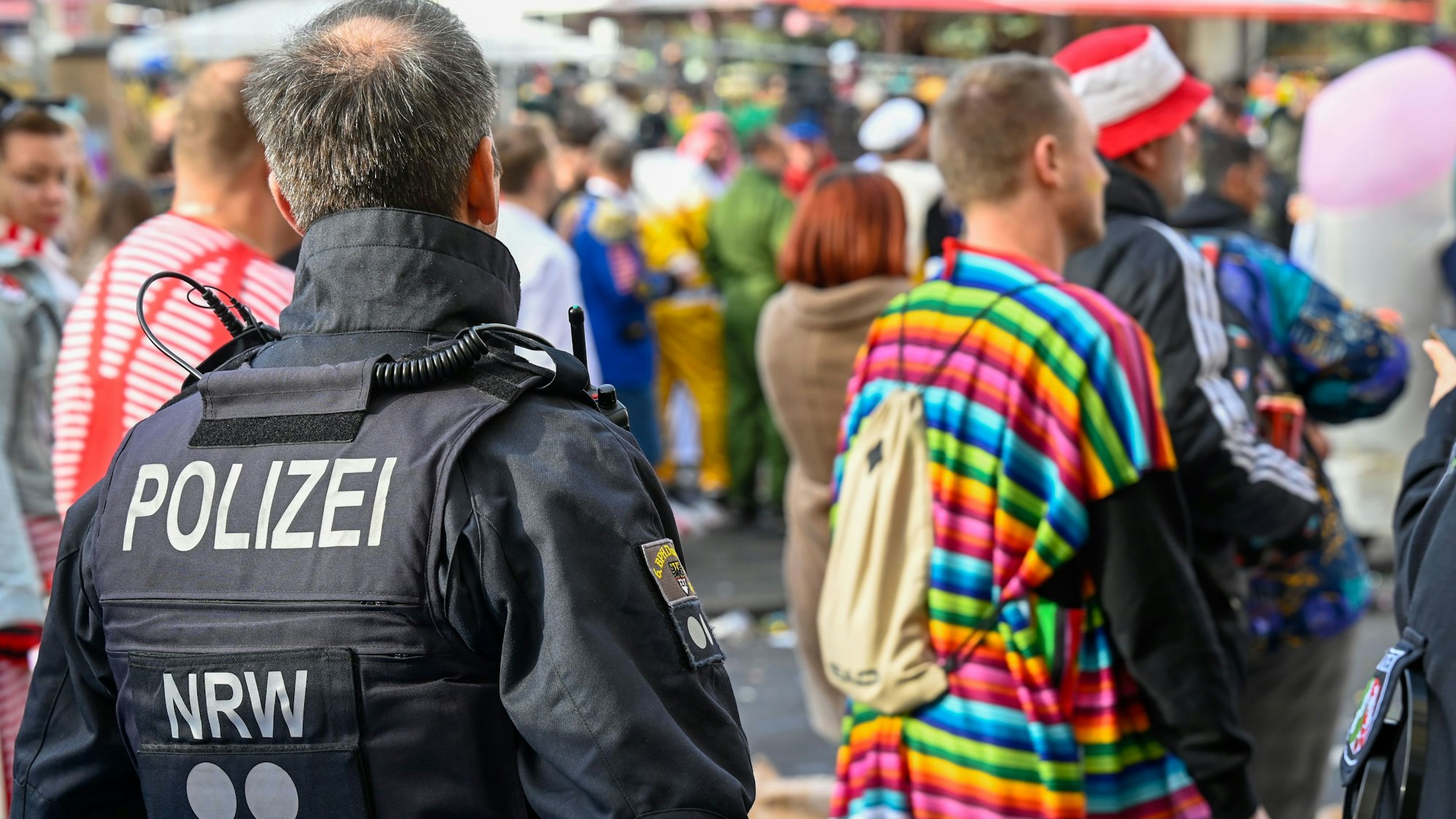 Ein Polizist beobachtet verkleidete Menschen an Karneval in Köln.