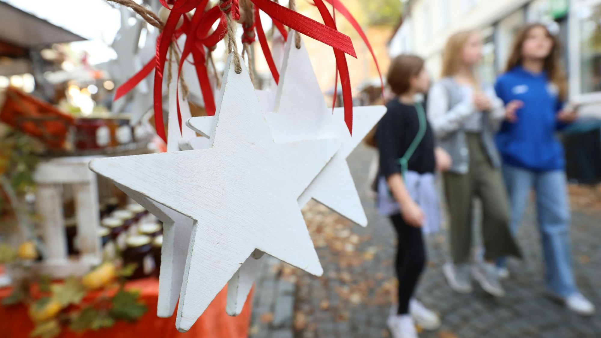 Weiße Sterne aus Holz mit roten Bändern hängen an einem Stand auf dem Martinimarkt. Im Hintergrund gehen Menschen daran vorbei.
