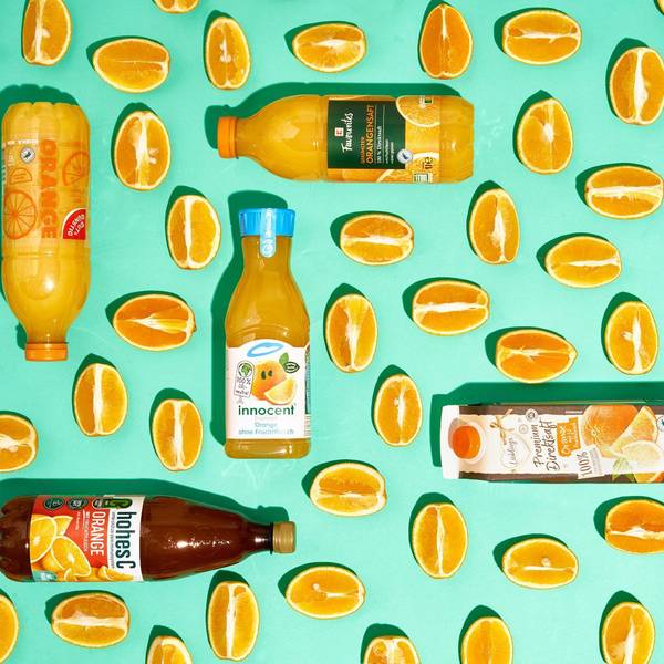 Sechs Flaschen mit Orangensaft zwischen Orangenspalten