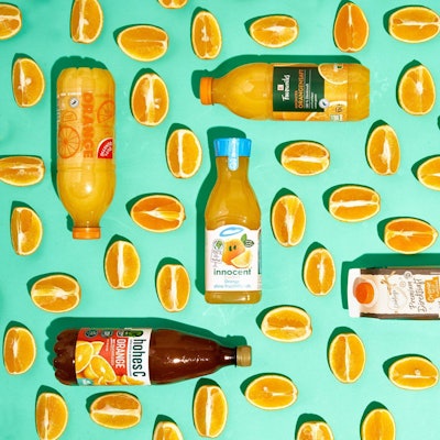 Sechs Flaschen mit Orangensaft zwischen Orangenspalten