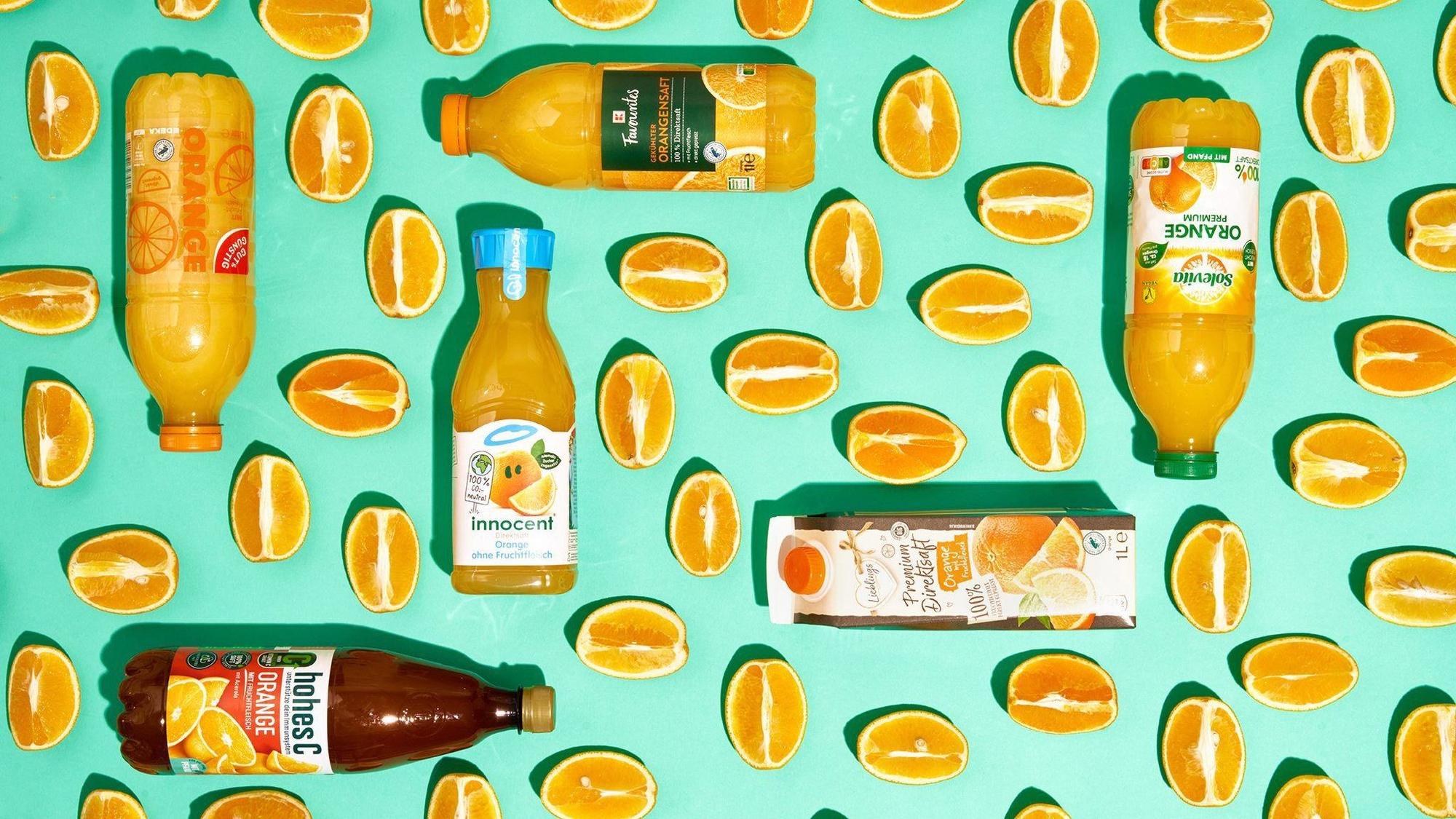 Sechs Flaschen mit Orangensaft zwischen Orangenspalten