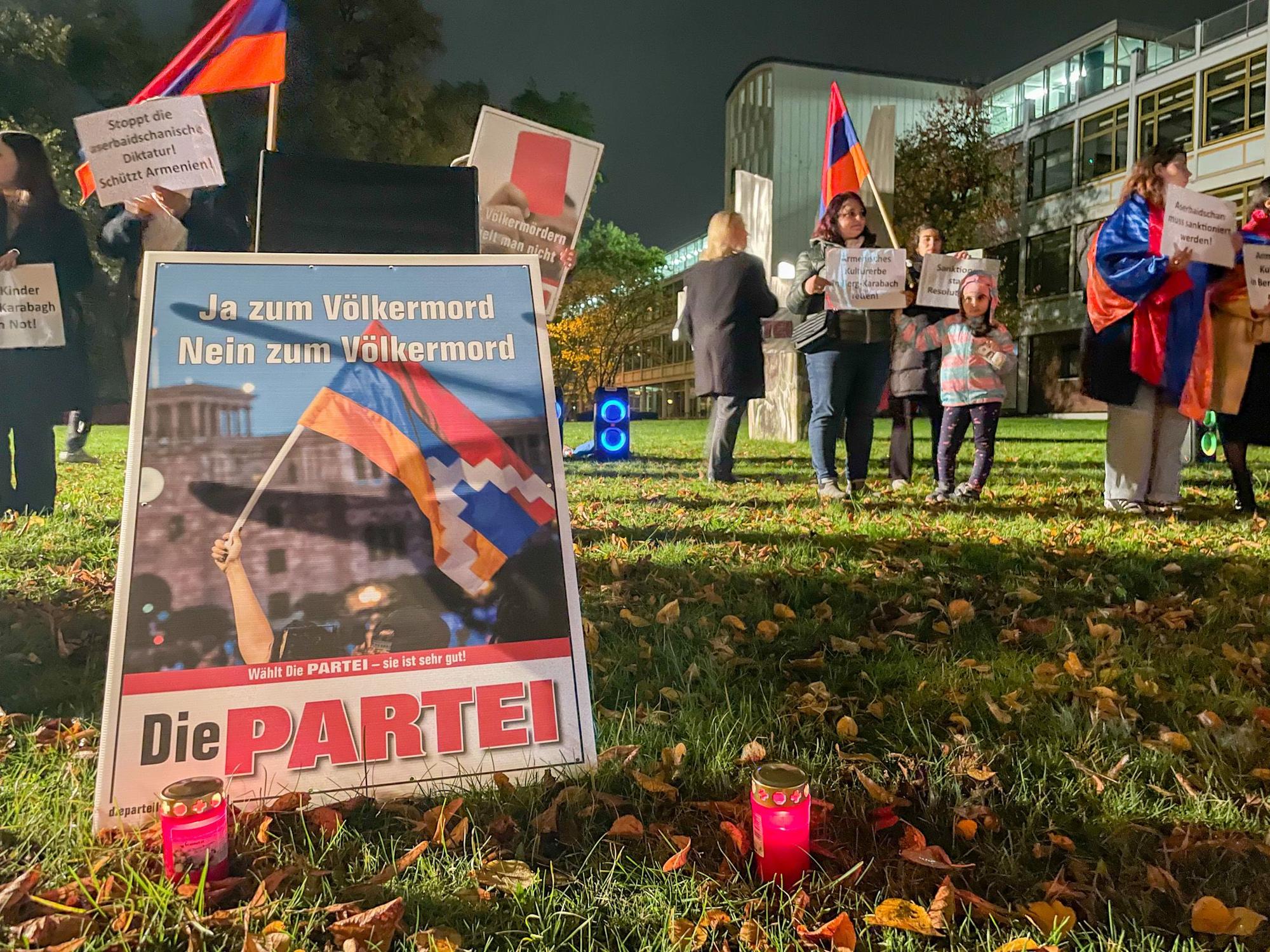Ein Schild von Die Partei, dahinter Demonstrierende.