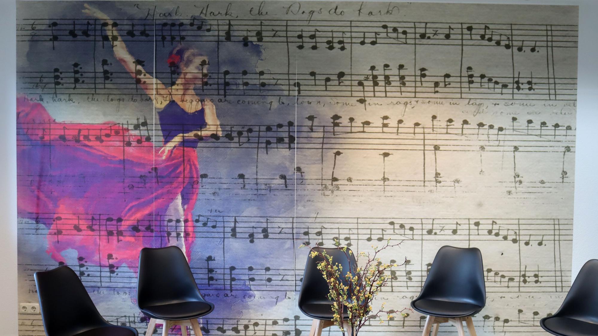 Ein Wandbild in der Tanzschule zeigt die Noten für ein Musikstück. Vor der Wand stehen fünf Stühle.