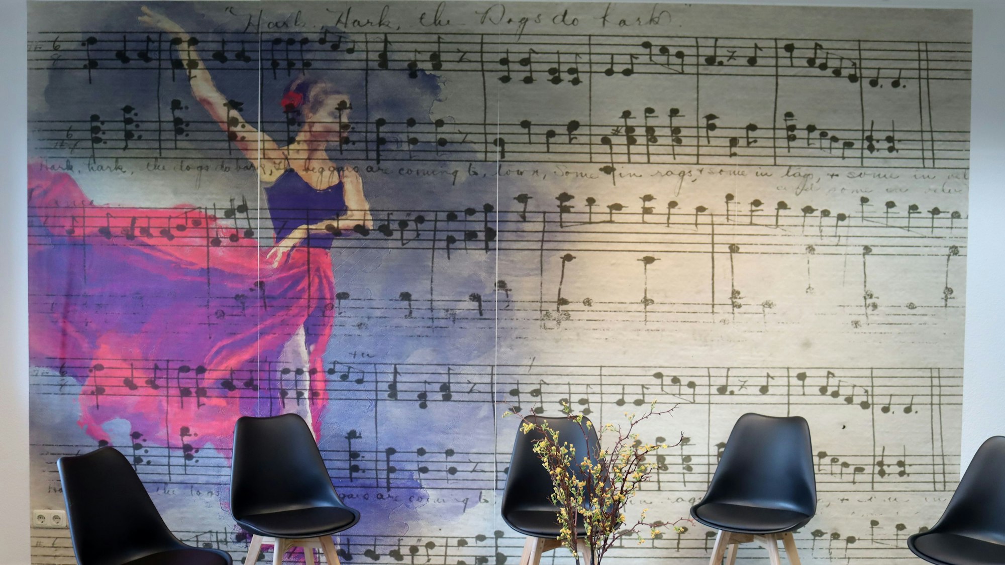 Ein Wandbild in der Tanzschule zeigt die Noten für ein Musikstück. Vor der Wand stehen fünf Stühle.