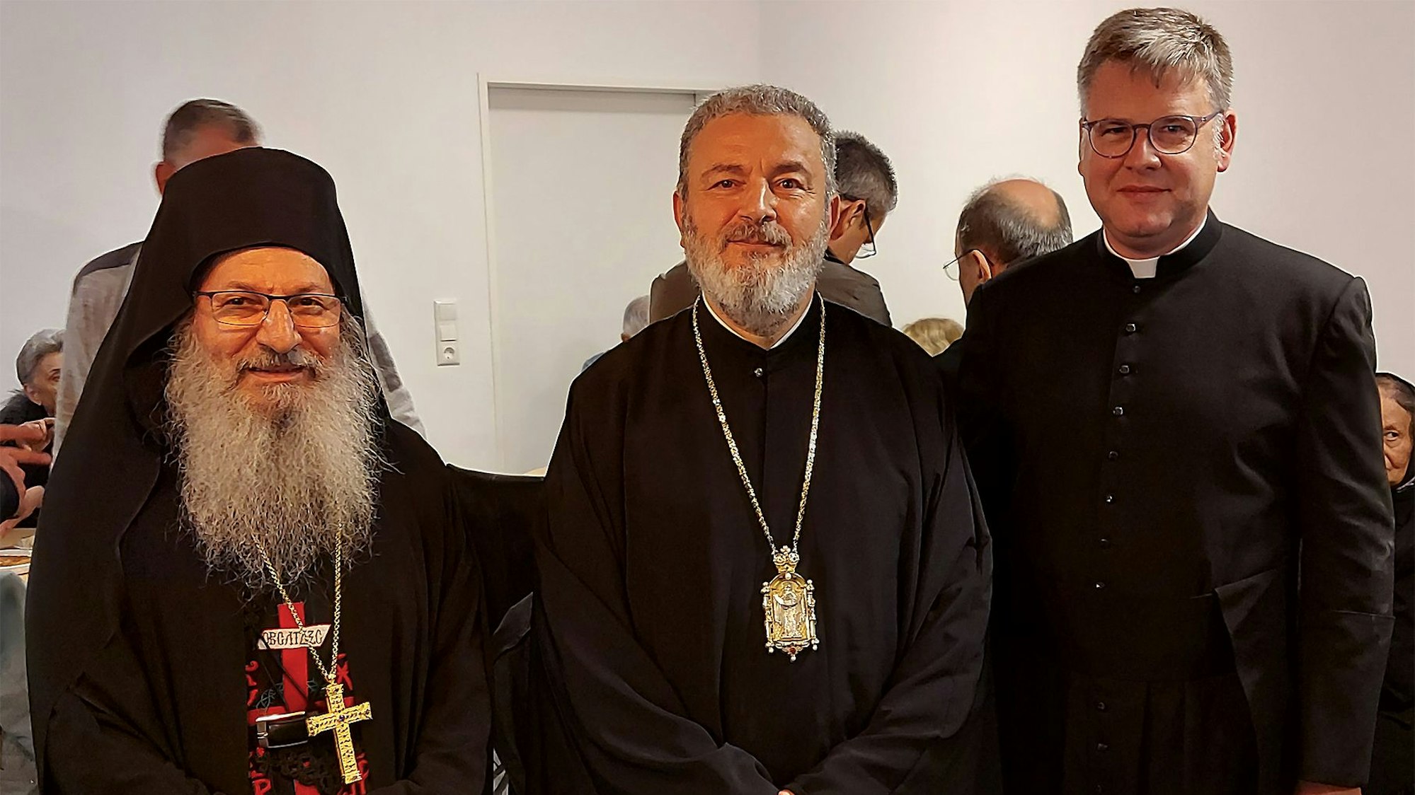 Drei Geistliche, alle drei schwarz gekleidet, stehen nebeneinander.