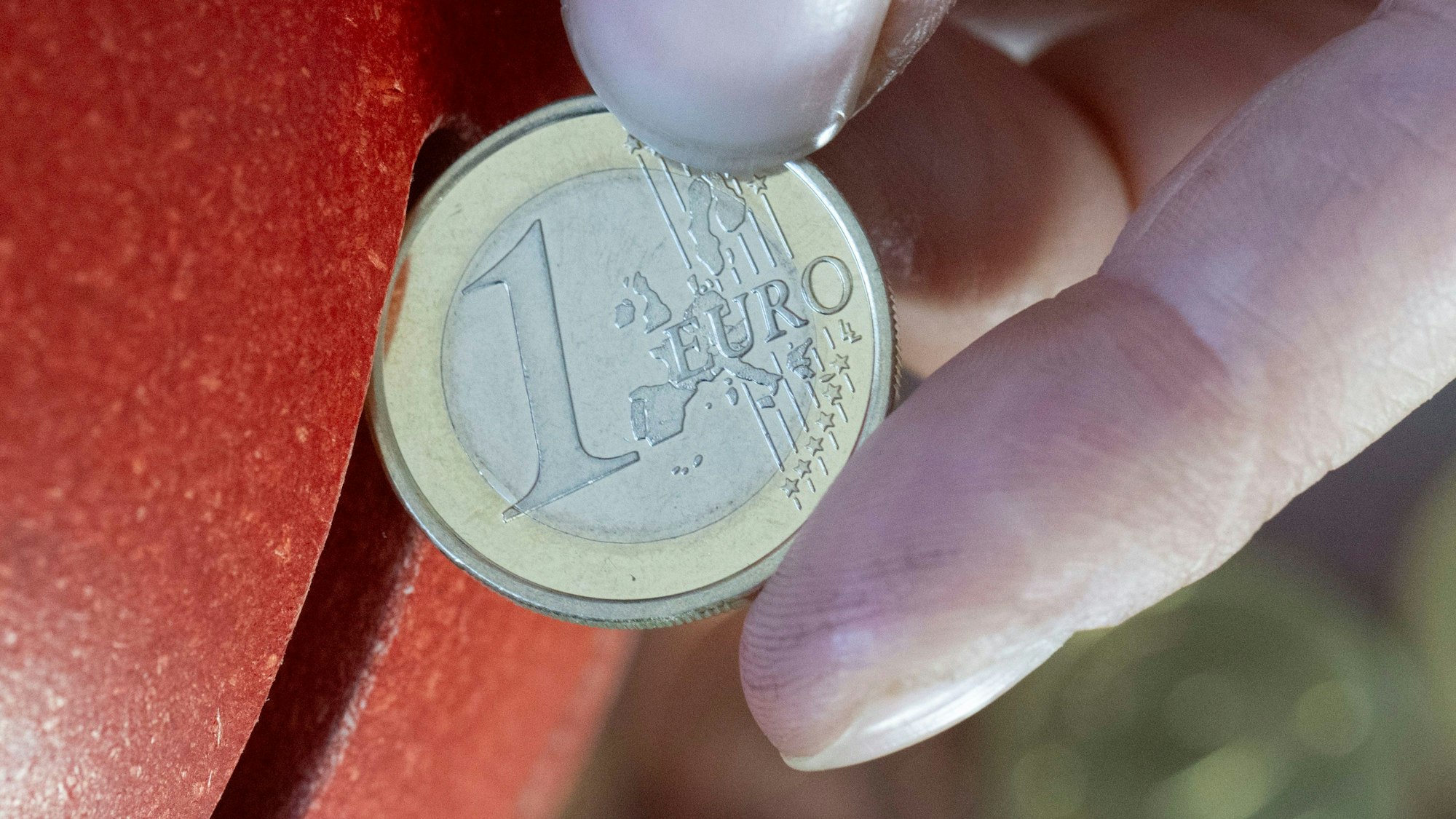 Eine Frau steckt eine 1-Euro-Münze in ein Sparschwein.