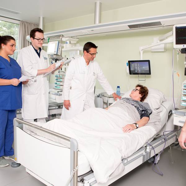 Ärzte stehen um ein Krankenbett herum, darin liegt eine Patientin.