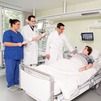 Ärzte stehen um ein Krankenbett herum, darin liegt eine Patientin.