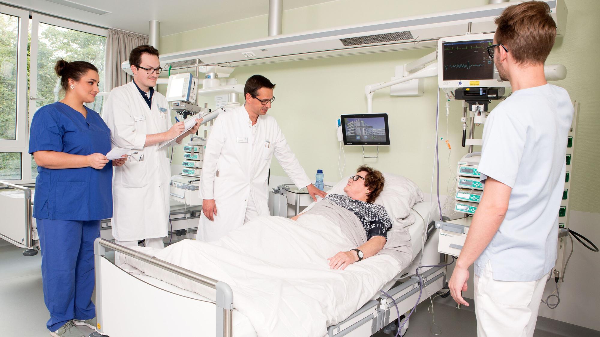 Ärzte stehen um ein Krankenbett herum, darin liegt eine Patientin.