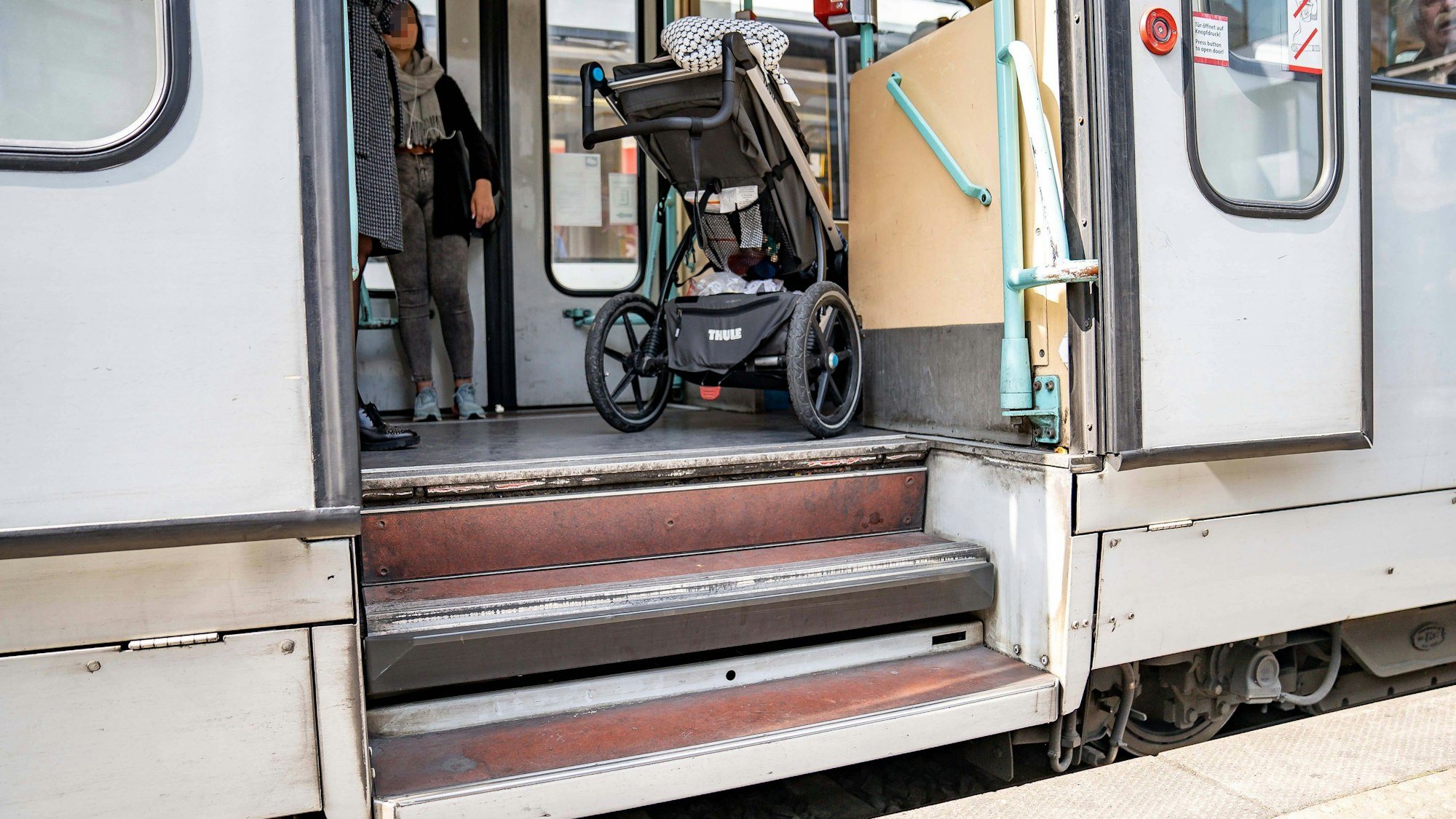 Das Foto zeigt einen Straßenbahnausstieg mit zwei Stufen. Vor der oberen Stufe steht ein Kinderwagen. Für Kinderwagen und Menschen im Rollstuhl sind derartige Ausstiege aus öffentlichen Verkehrsmitteln nur schwer zu bewältigen.