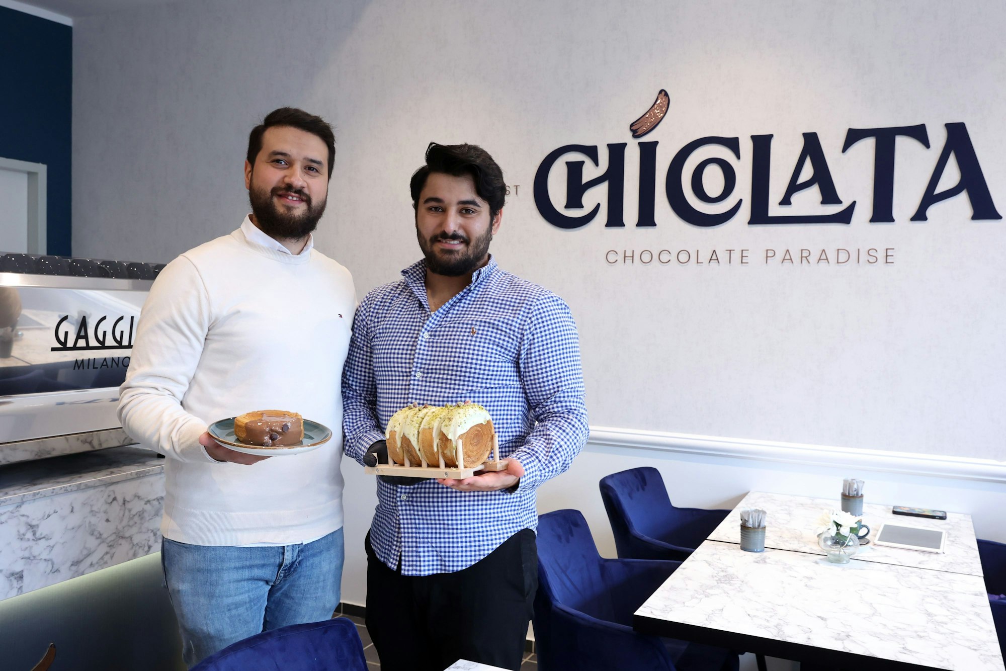 Zwei Männer halten Teller mit Gebäck in den Händen und blicken in die Kamera.