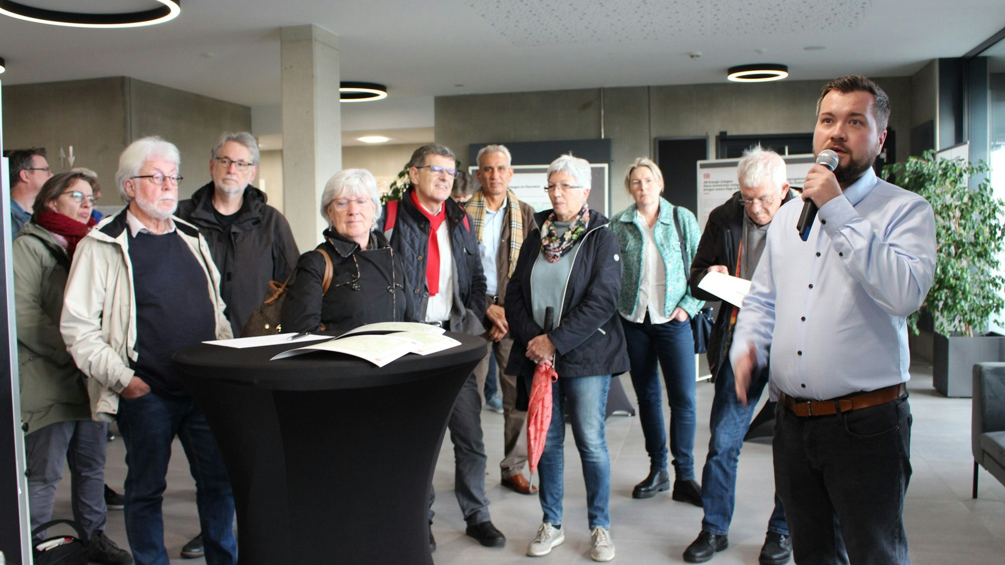 Projektleiter Nikolai Kopnow hält ein Mikrofon in der Hand, hinter ihm stehen einige der Besucher des DB-Bürgerdialogs.