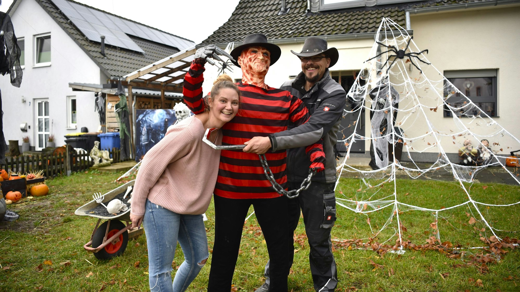 Mareike und Sascha Zahnke stehen in einem Vorgarten, um sie herum lauter gruselige Figuren, Spinnweben und Halloween-Deko.