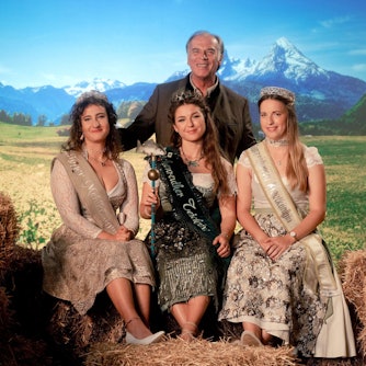 Die Königinnen sitzen, hinter ihnen thront Josef Gehrling als ihr Patriarch. Rechts und links neben ihnen Stroh und ein Milchkübel, im Hintergrund eine bayrische Landschaft. Das Bild ist bewusst überzeichnet und spielt mit bayrischen Klischees.