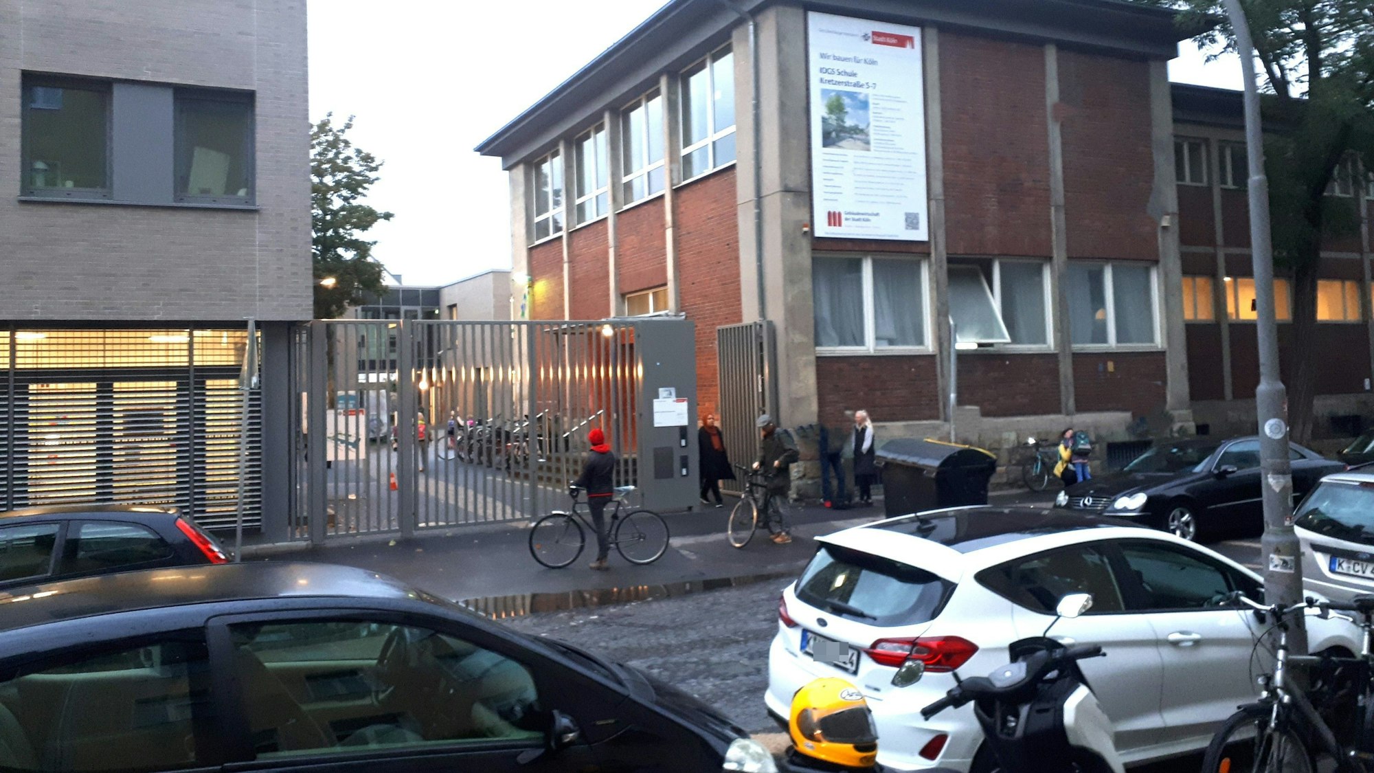 Fahrräder und Autos stehen vor dem Schuleingang.