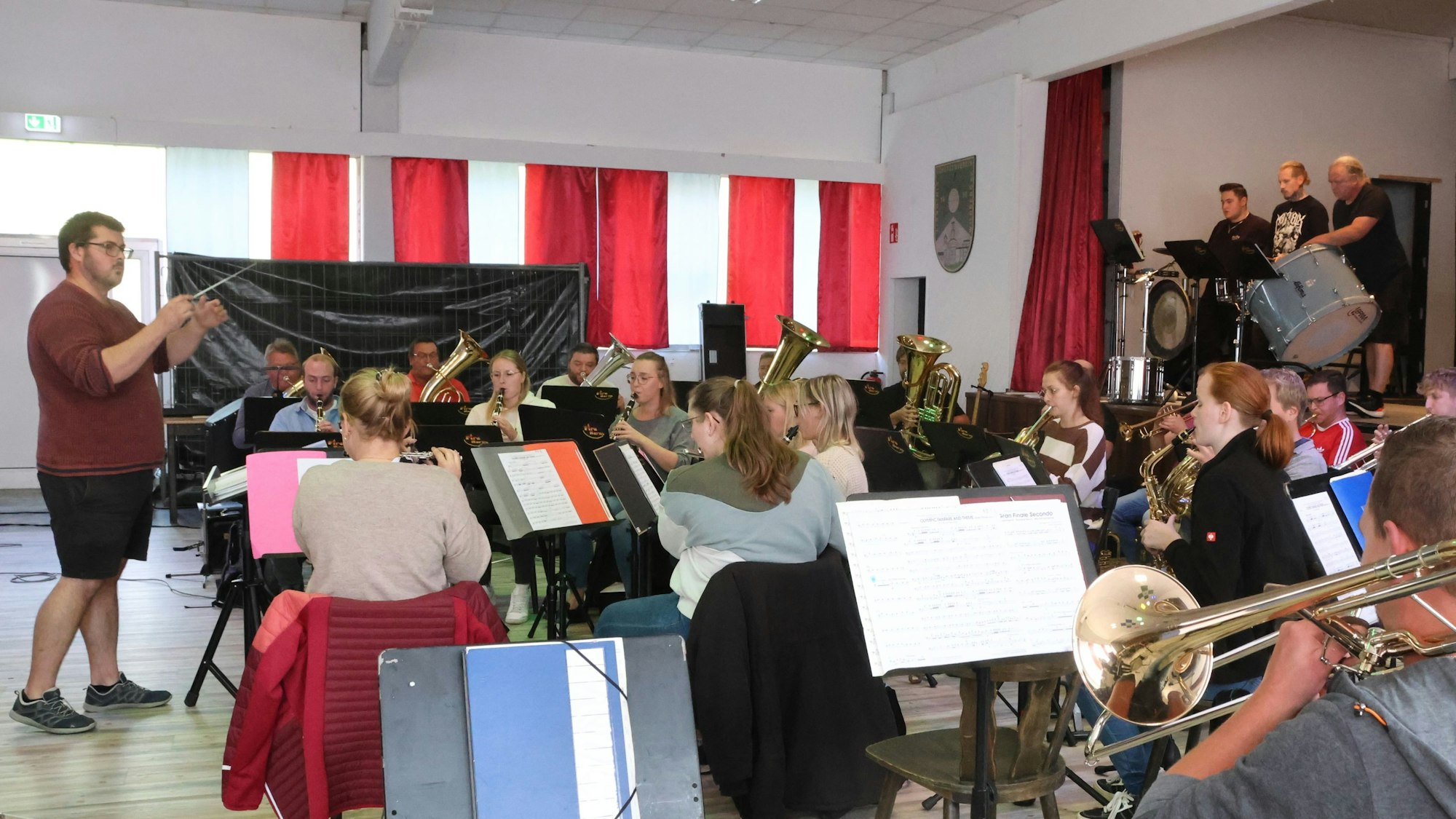 Ein Blasorchester und sein Dirigent proben in einem Saal.