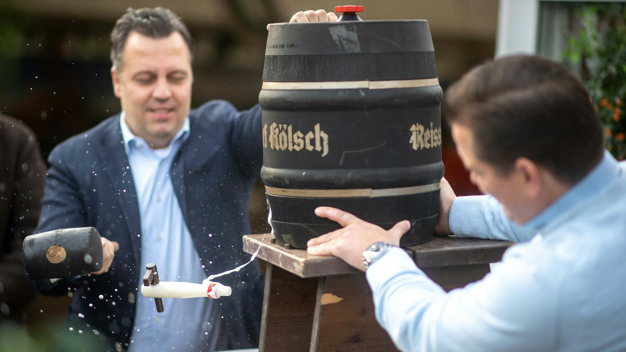 Das Bild zeigt den Bürgermeister, wie er sich beim Fassanstich versucht. Der Zapfhahn fliegt nach dem Schlag mit dem Hammer aber durch die Luft.