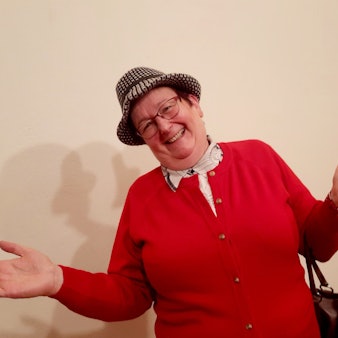 Ulrike Bömer posiert in einer roten Strickjacke mit ausgebreiteten Händen in ihrer Paraderolle als Erna Schabiewski.