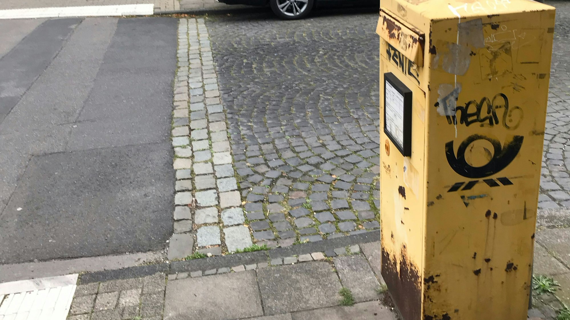 Ein total rostiger Briefkasten steht auf dem Bürgersteig an einer Straße.