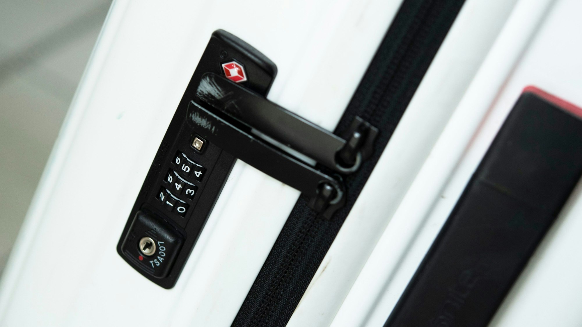 Ein weißer Koffer mit einem schwarzen Schloss steht auf dem Boden.