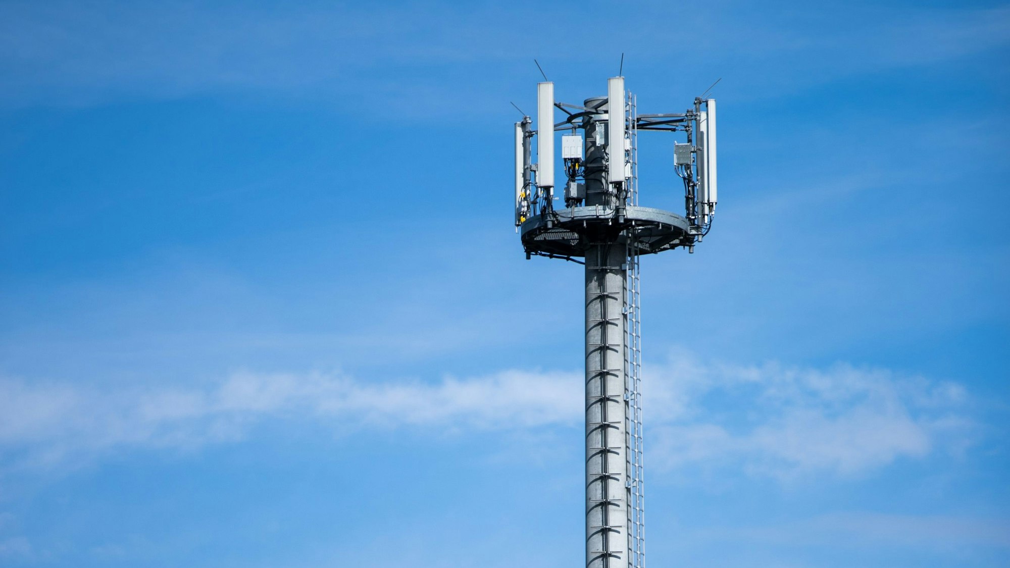 Ein Mobilfunkmast ragt in den blauen Himmel.