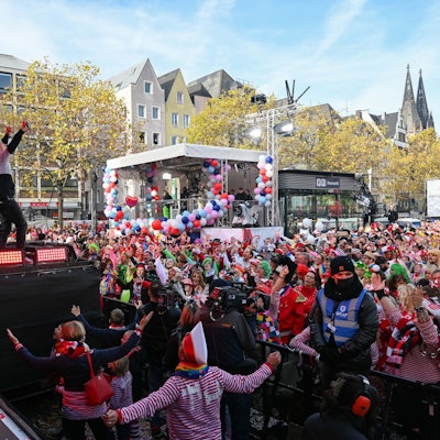 Kasalla stehen auf der Bühne auf dem Heumarkt, vor ihnen feiern Tausende Jecken.