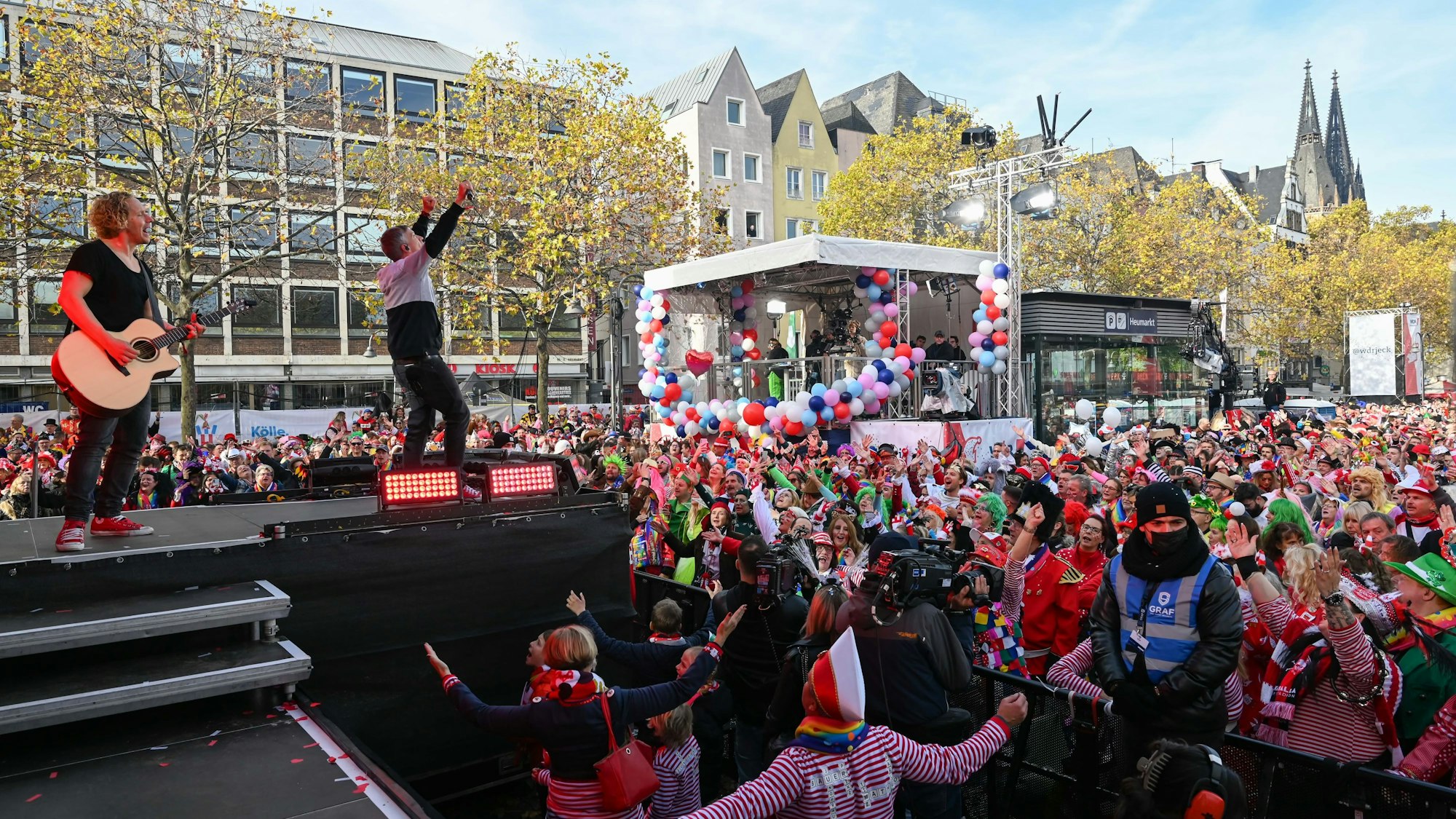 Kasalla stehen auf der Bühne auf dem Heumarkt, vor ihnen feiern Tausende Jecken.