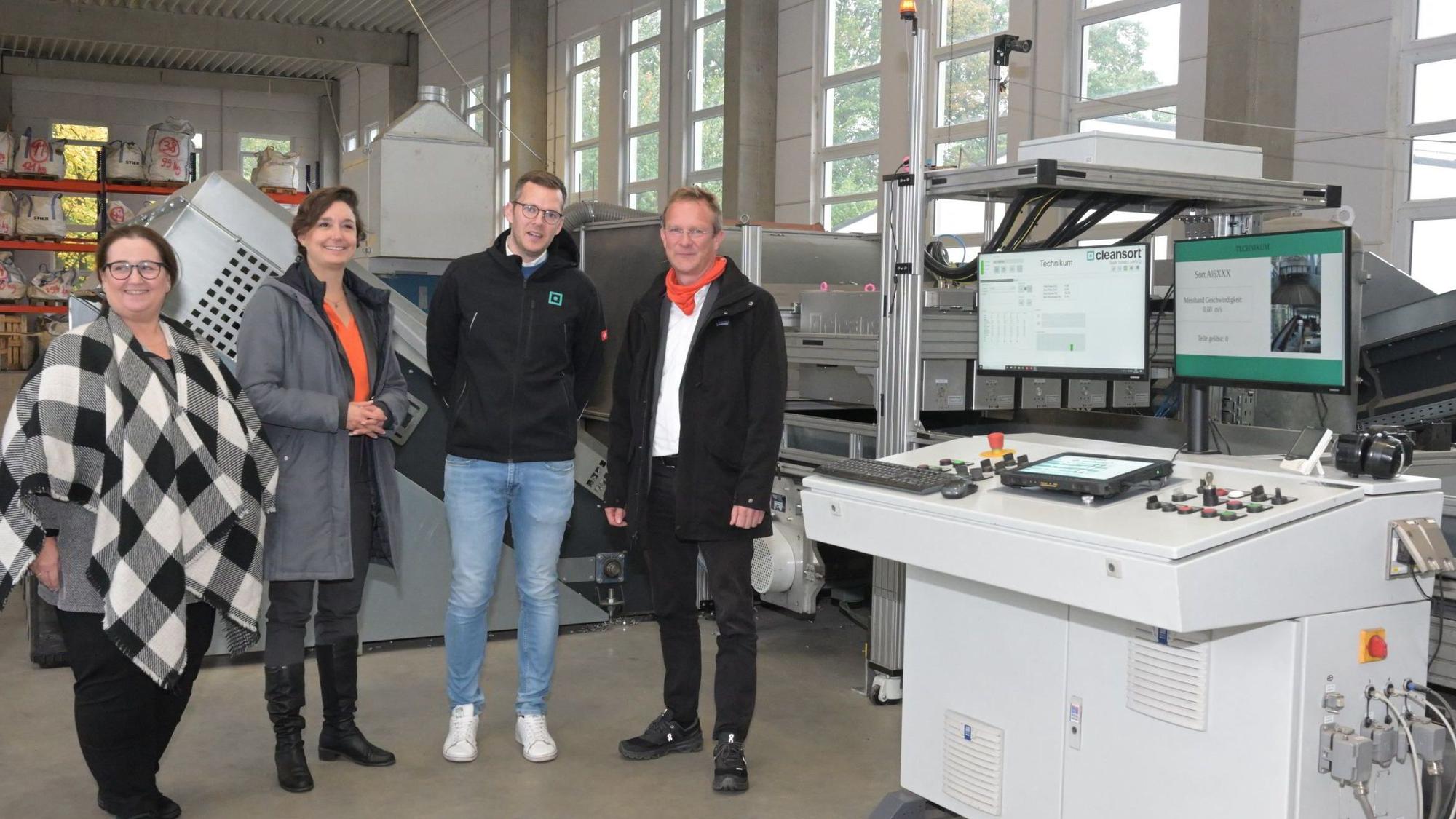 Eine Gruppe von Personen steht an einer technischen Anlage für das Recyceln von Aluminium-Schrott.
