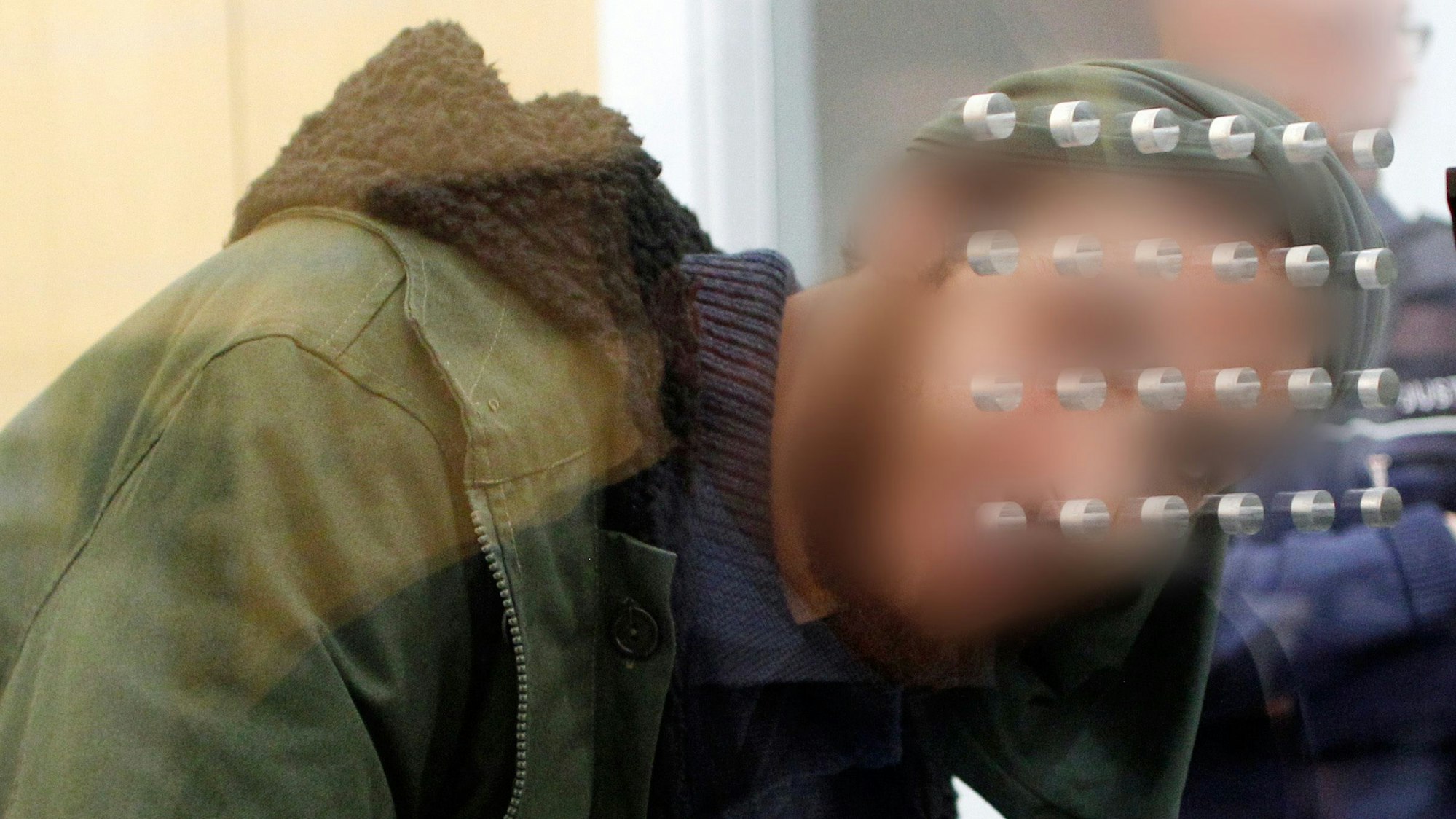 Der Angeklagte Tarik Süleyman S. wartet hinter einer Sicherheitsscheibe am 22.12.2016 vor dem Oberlandesgericht in Düsseldorf (Nordrhein-Westfalen) auf den Prozessbeginn. Der 23-jährige Deutsche soll drei Jahre lang in Syrien gewesen sein und sich im Januar 2014 der Terrormiliz Islamischer Staat angeschlossen haben. Die Bundesanwaltschaft wirft ihm unter anderem vor, sich an Kampfeinsätzen und Grenzkontrollen beteiligt zu haben. (ACHTUNG - Das Gesicht des Angeklagten und das Gesicht des Justizbeamnten wurde auf Verfügung des Gerichts gepixelt.) Foto: Roland Weihrauch/dpa ++ +++ dpa-Bildfunk +++